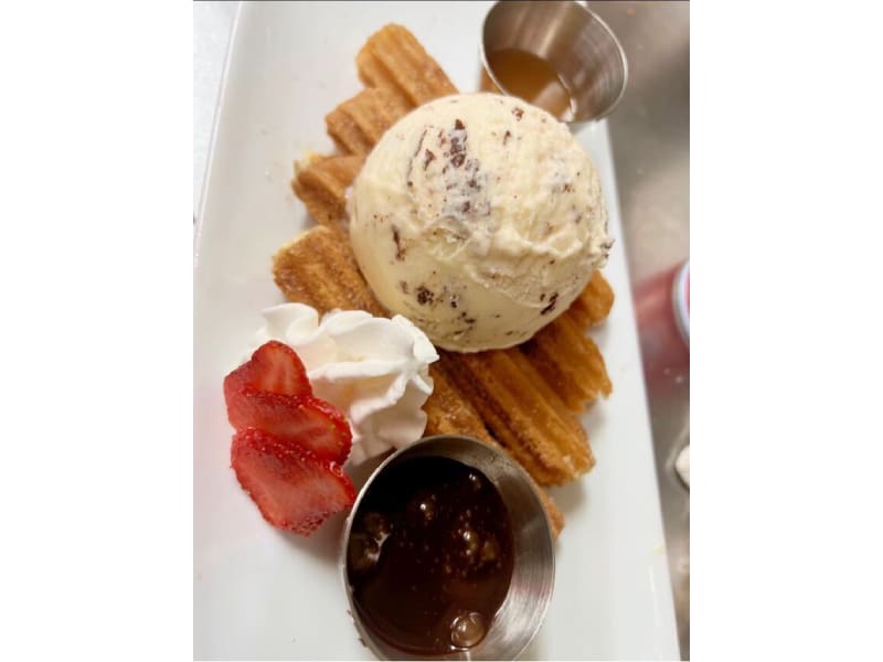 A plate of food with ice cream, strawberries and churro.